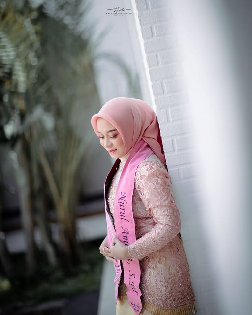 Potret wisudawati bersandar di dinding putih