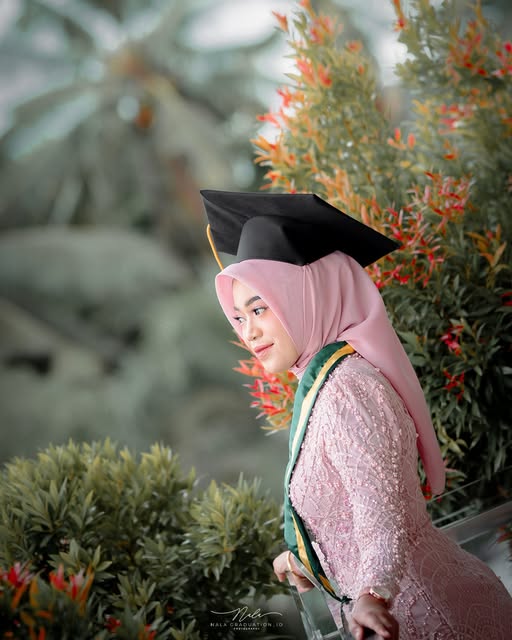 Wisudawati berhijab merah muda dengan toga di taman, foto Nala Graduation